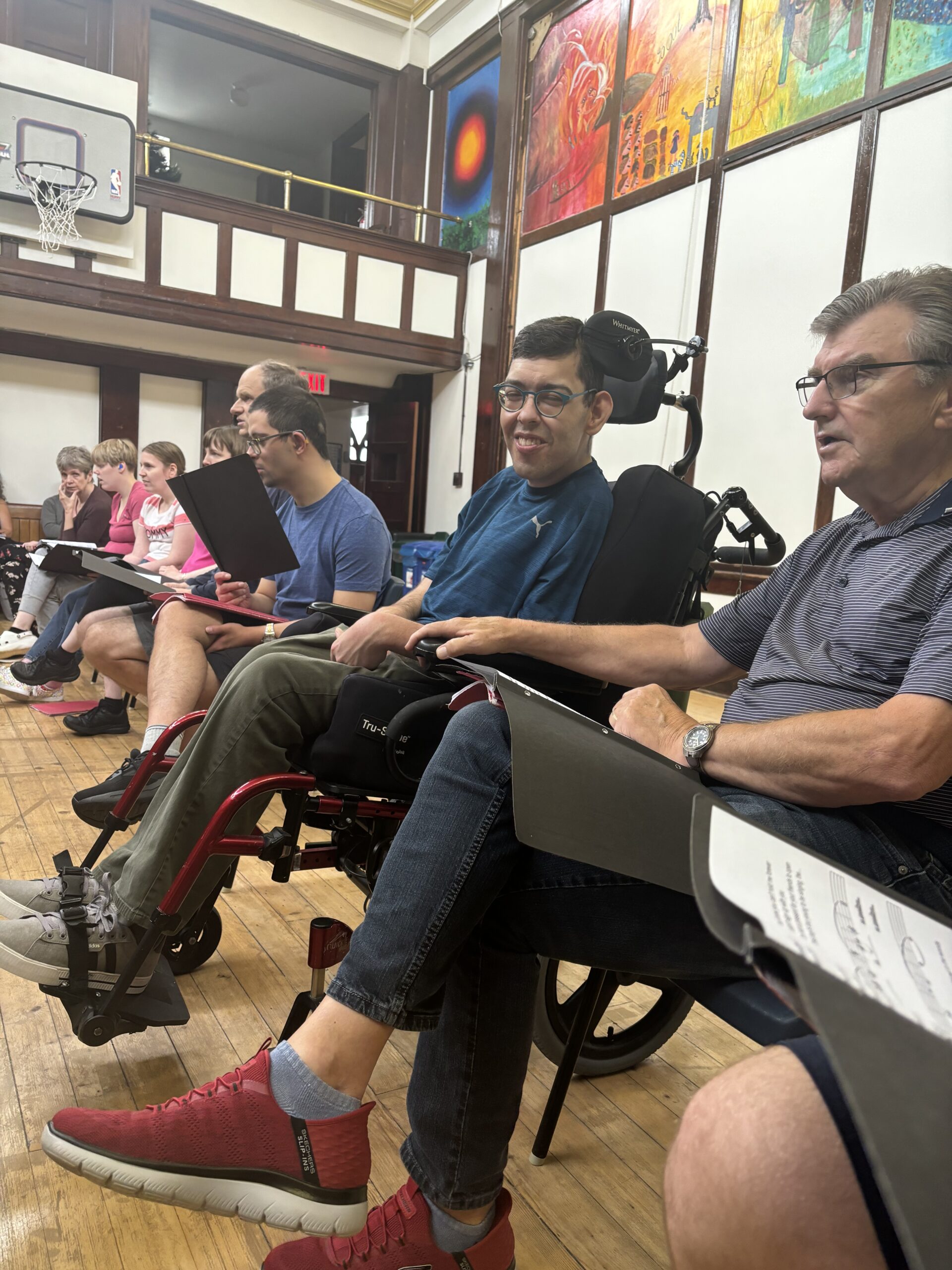 group of people sitting in chairs together, reading music and singing at a choir event.